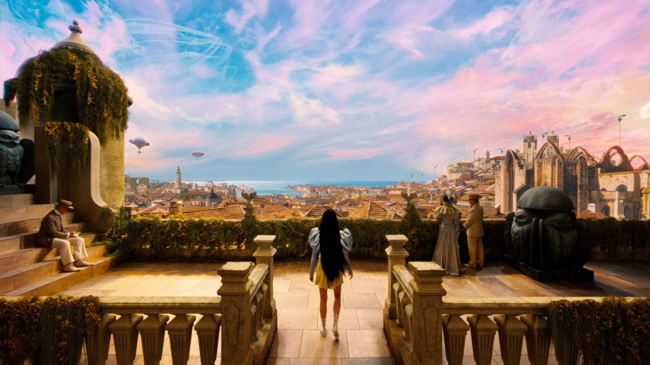 A woman with long, jet-black hair, seen from behind, wanders onto a pavilion in a steampunk Lisbon as the vibrant blues and purples of the sky stretch out in front of her