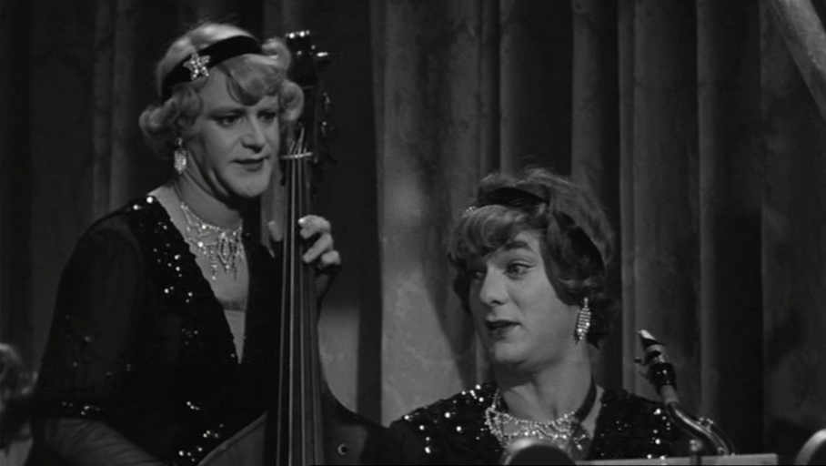 Two cross-dressing white men in sparkling dresses playing instruments in black and white