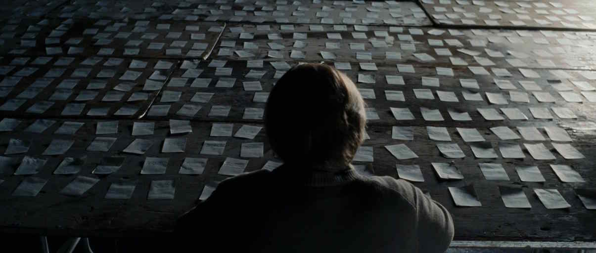 A man with his back to the camera sits in front of scores of post-it notes laying on a table