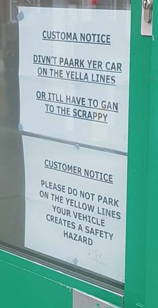 Two paper signs, the top one reading "Customa notice: Divn't paark yer car on the yella lines or itll have to gan to the scrappy", the bottom reading "Customer notice: Please do not park on the yellow lines / your vehicle creates a safety hazard"